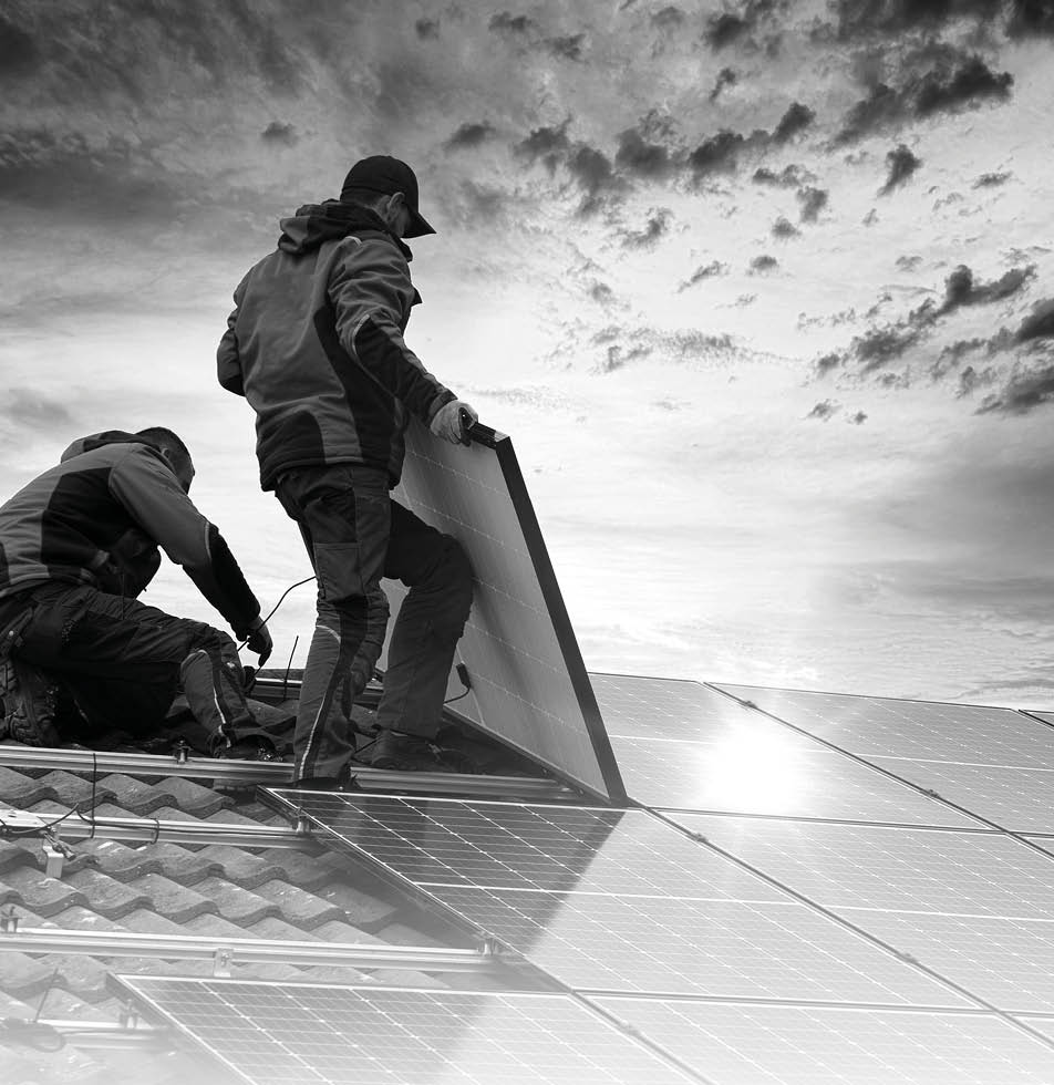 B&W image of people fitting in a solar panel on a roof 